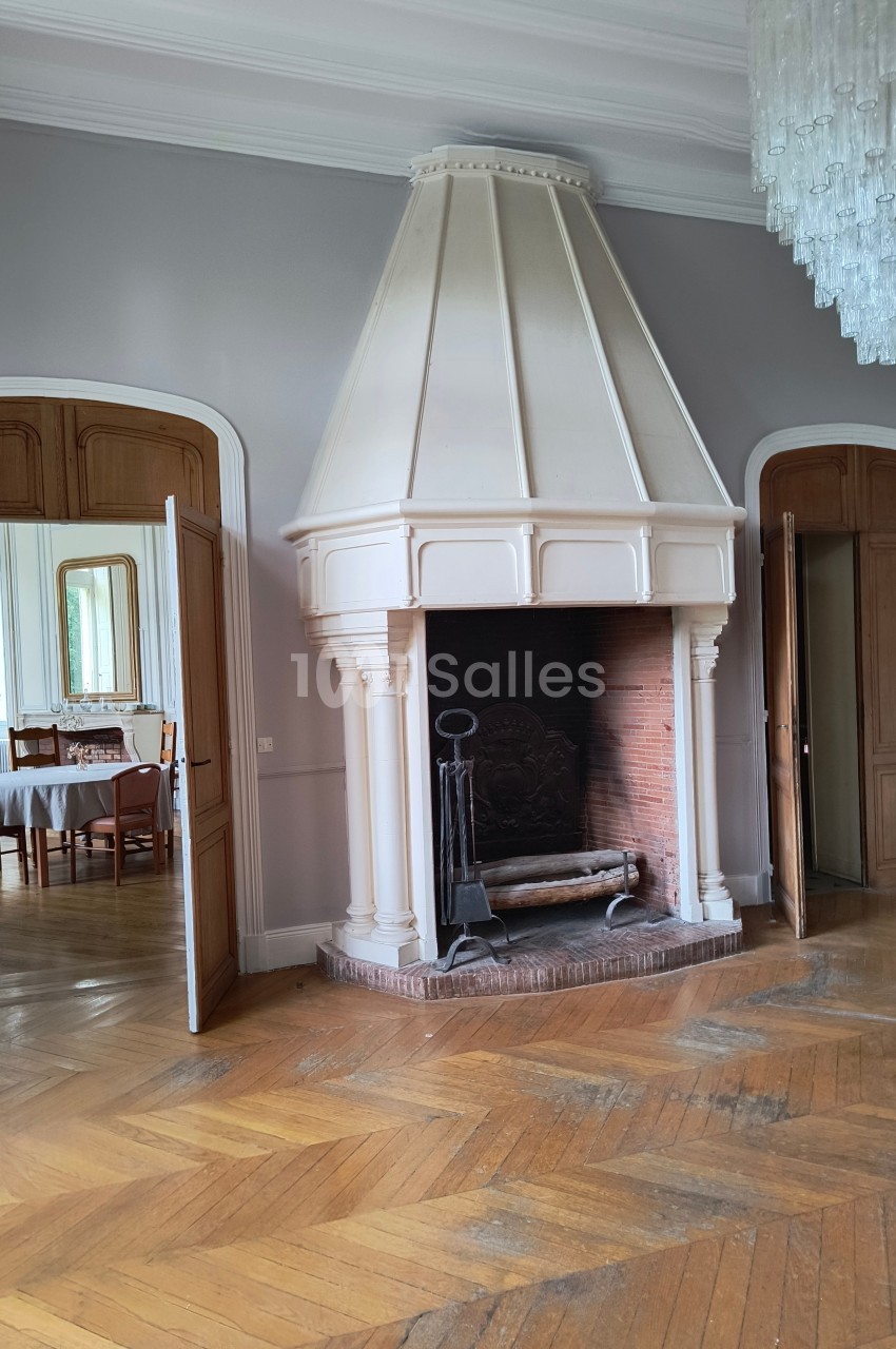 Cheminée ancienne en pierre blanche dans une pièce avec parquet en bois, portes ouvertes donnant sur une salle à manger.