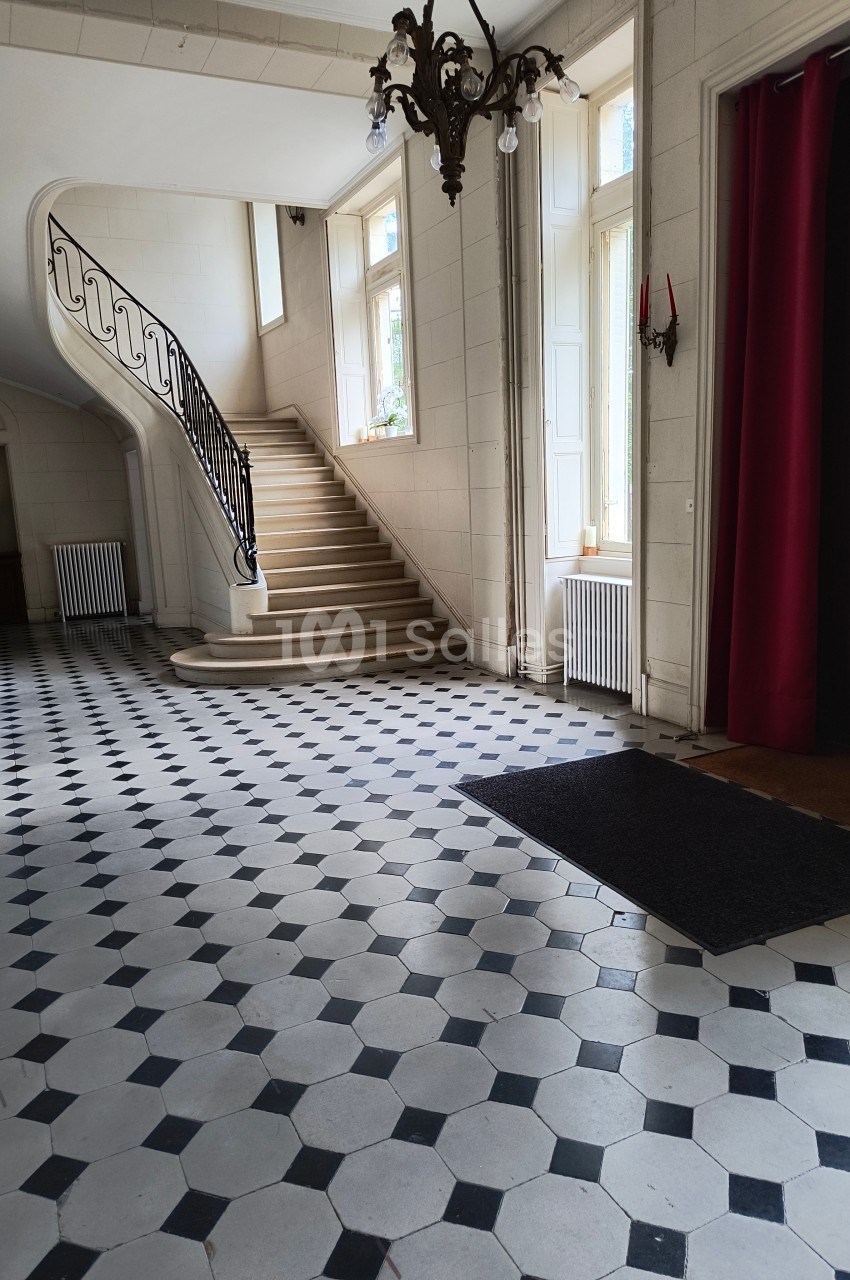 Hall d'entrée lumineux avec sol en carreaux noirs et blancs, escalier en colimaçon et grandes fenêtres.