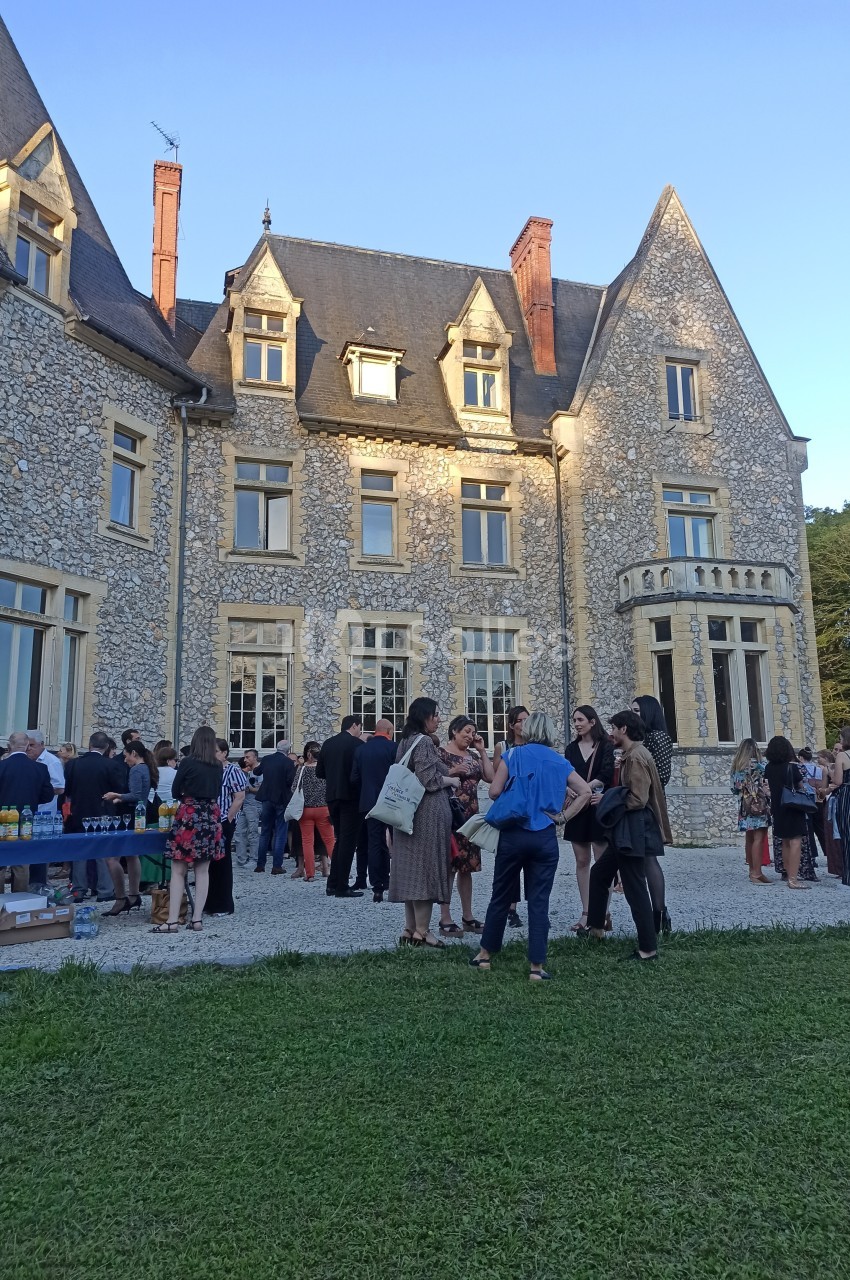 Groupe de personnes rassemblées devant un château en pierre lors d'un événement en plein air par temps ensoleillé.