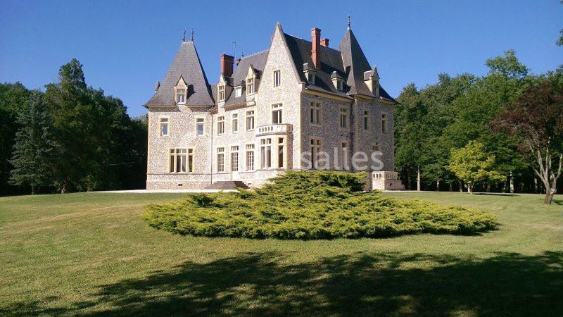 Château en pierre entouré d'un grand jardin verdoyant, avec un ciel bleu dégagé en arrière-plan.