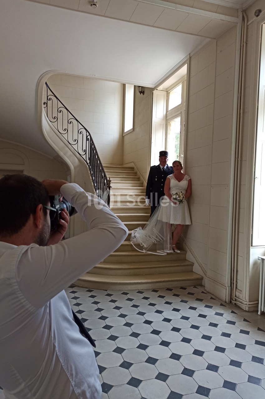Un photographe capture un couple de mariés posant près d'un escalier dans un intérieur lumineux.