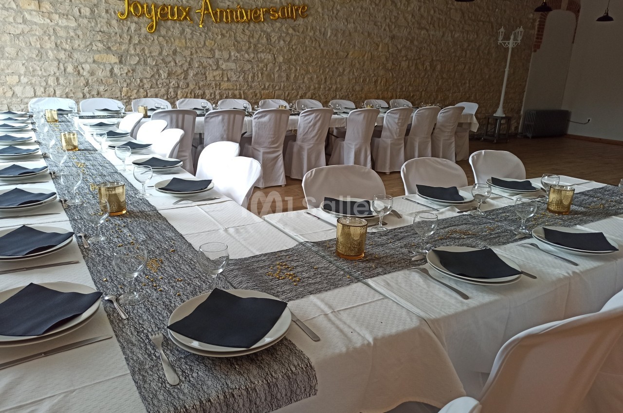 Salle décorée pour un anniversaire avec tables dressées, nappes blanches, serviettes noires et bougies dorées.