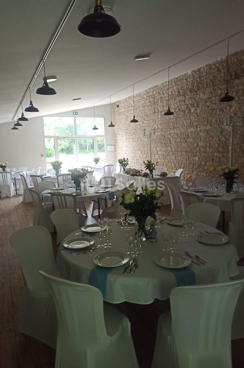 Salle de réception lumineuse avec tables rondes dressées, nappes blanches, chaises assorties et décoration florale.