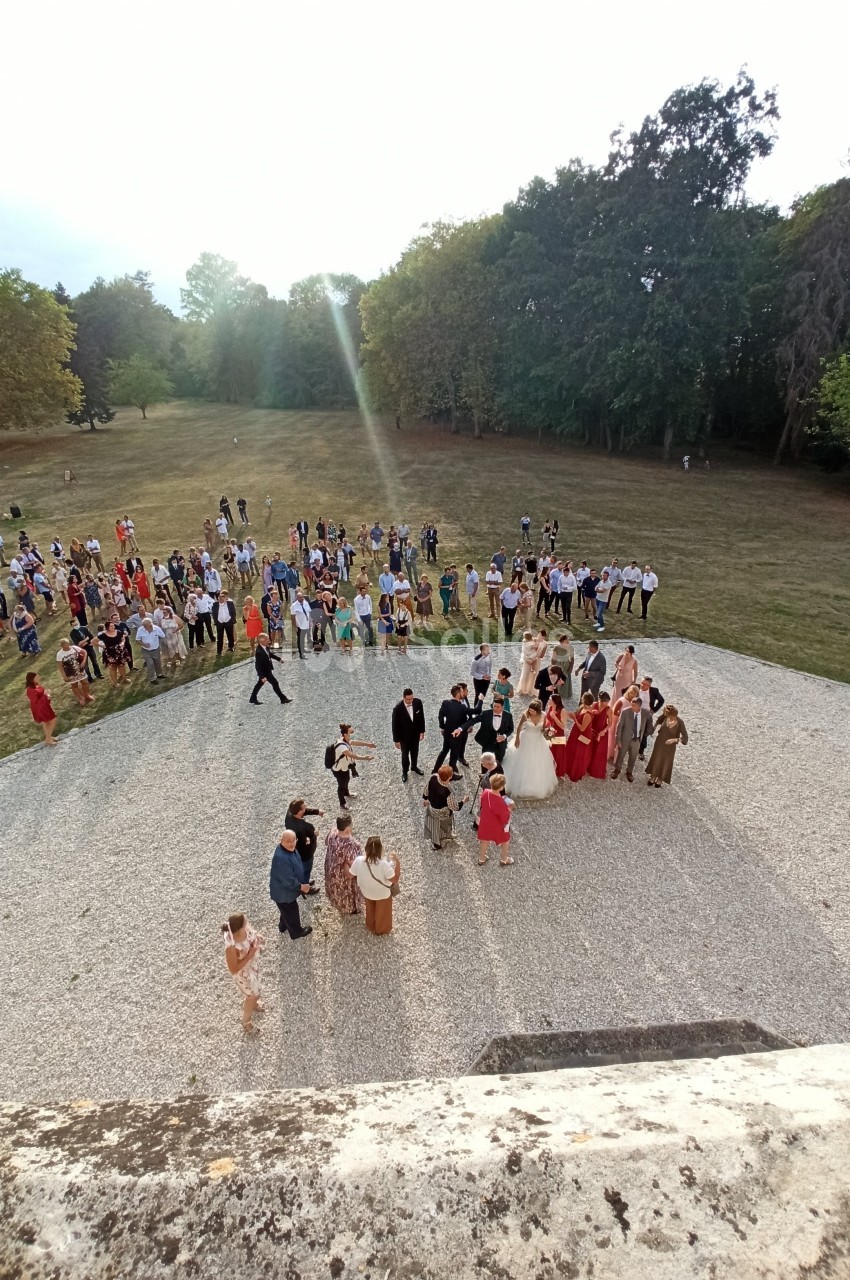 Groupe de personnes rassemblées en extérieur sur une esplanade, entourée de pelouse et d'arbres.