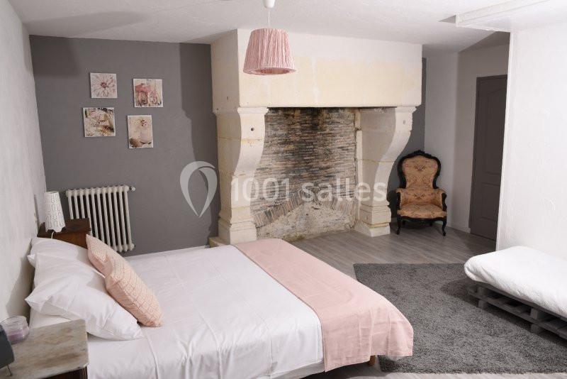 Chambre avec lit double, cheminée ancienne, fauteuil, décorations murales et éclairage doux dans un style chaleureux.