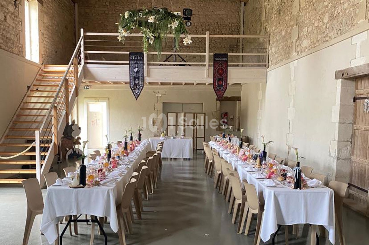 Salle de réception avec tables dressées pour un repas, décorations suspendues et murs en pierre apparente.