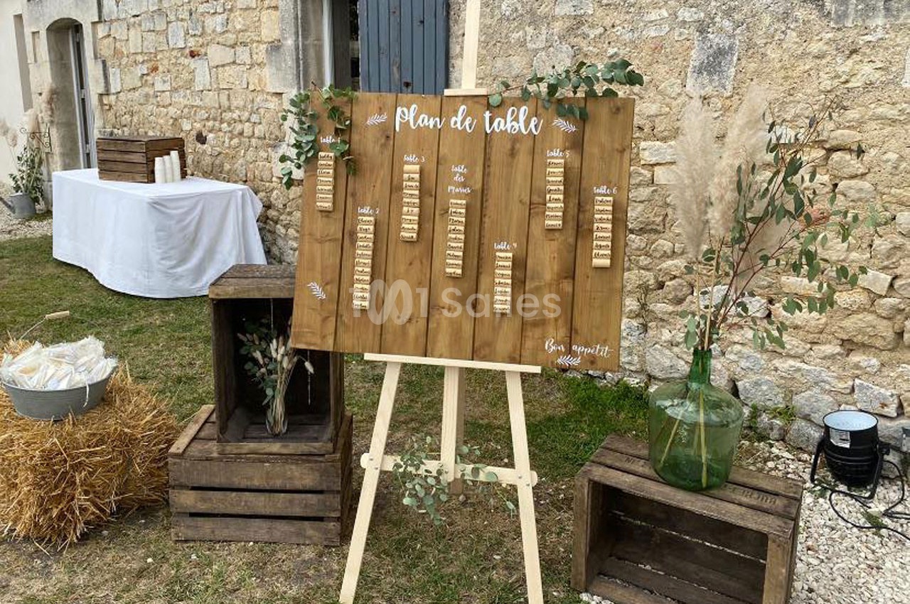 Plan de table en bois sur un chevalet, entouré de caisses en bois, décorations végétales et bottes de paille.