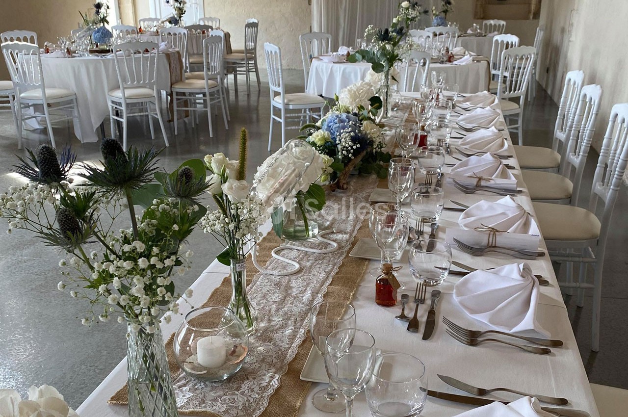 Tables élégamment dressées pour un événement, ornées de fleurs blanches et bleues, avec nappes blanches et chaises assorties.