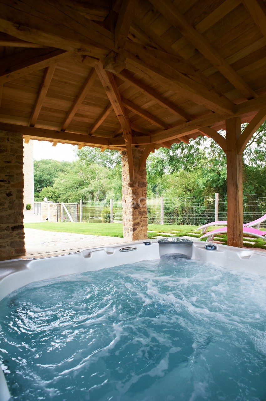 Vue d'un jacuzzi extérieur sous une pergola en bois, avec un jardin verdoyant en arrière-plan.
