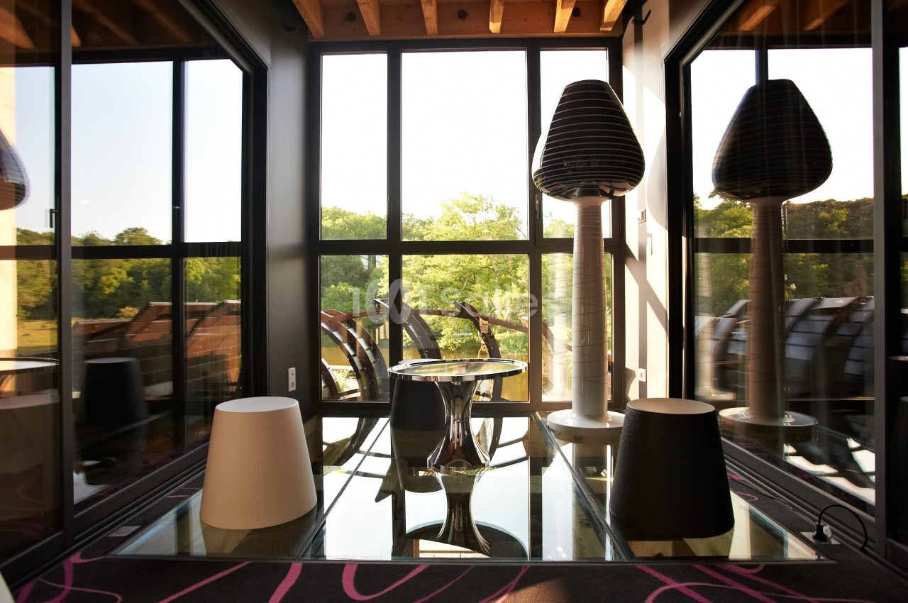Espace lumineux avec grandes baies vitrées, mobilier design et vue sur un paysage verdoyant.