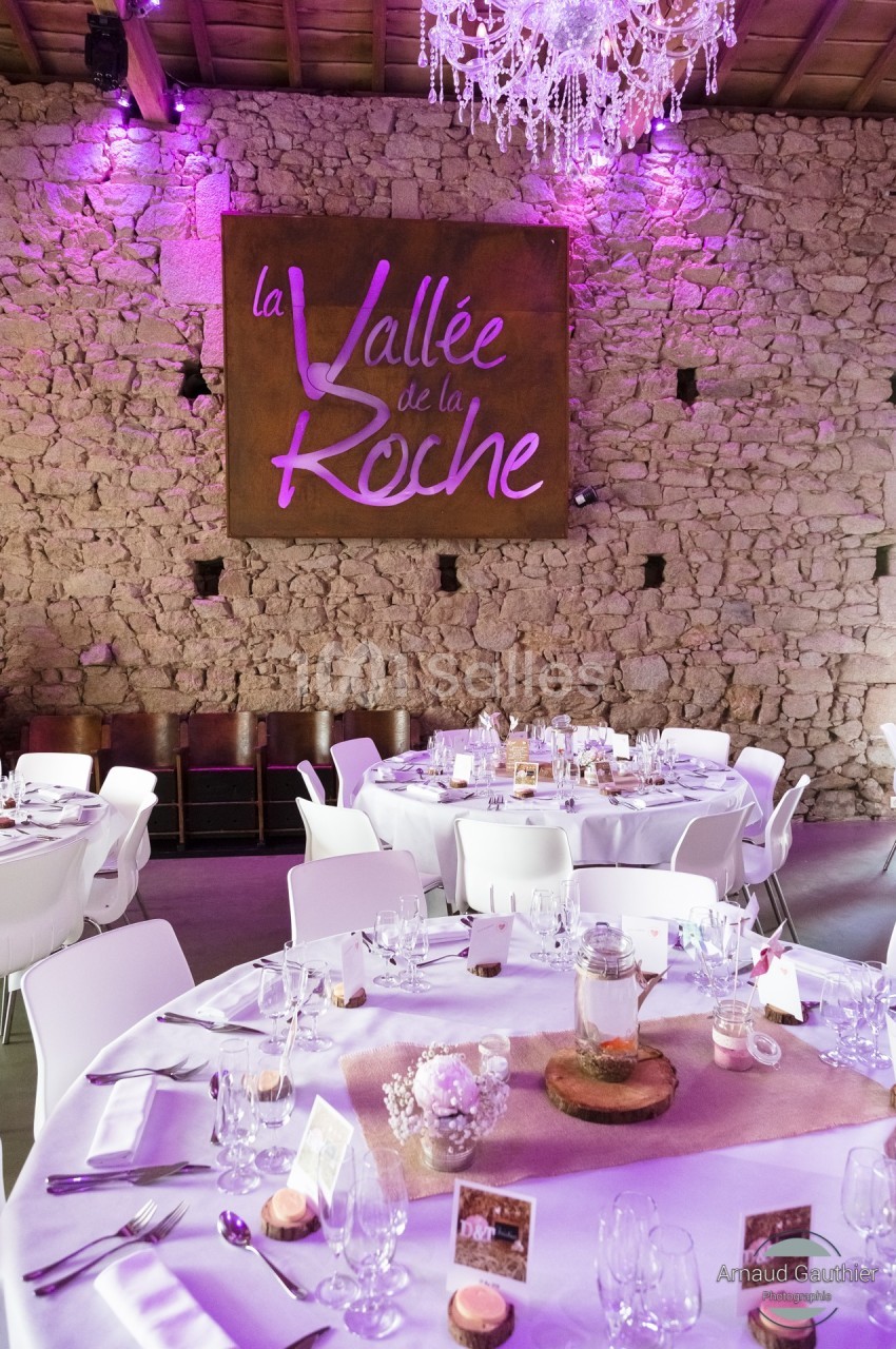 Salle de réception avec murs en pierre, tables dressées et un panneau lumineux indiquant ’La Vallée de la Roche’.