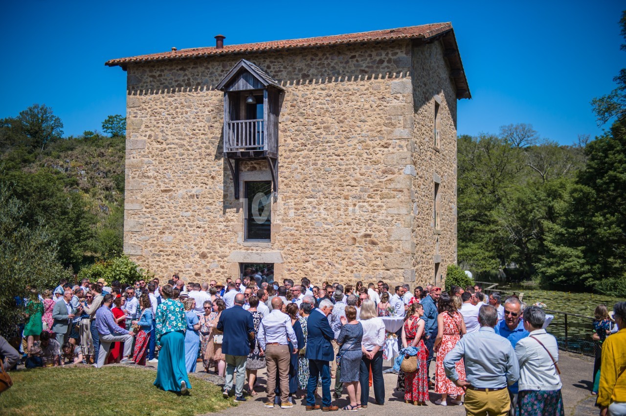 Groupe de personnes rassemblées devant un bâtiment en pierre sous un ciel bleu, entouré de verdure.