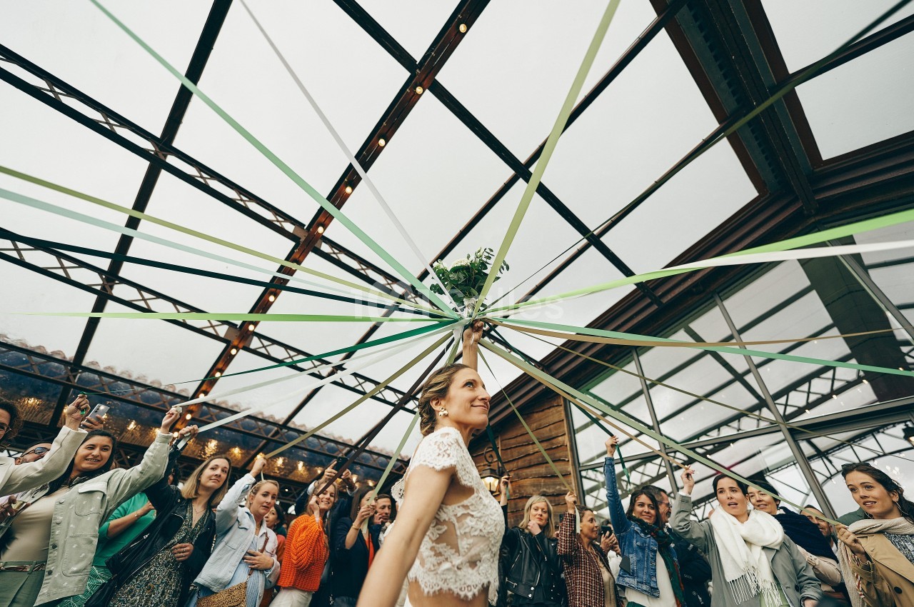Une femme danse sous des rubans tendus, entourée d'invités dans une salle lumineuse avec une verrière.