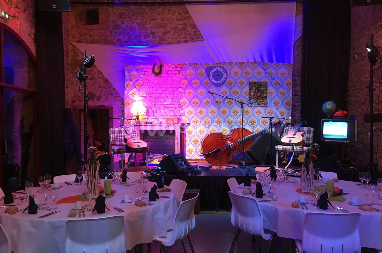 Scène décorée avec des instruments de musique, éclairages colorés et tables dressées pour un événement festif.