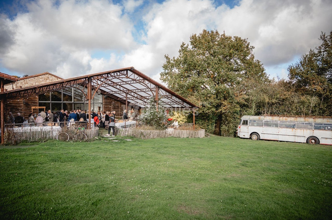Un groupe de personnes rassemblé devant un bâtiment en bois avec une structure métallique, près d'un bus ancien sur une…