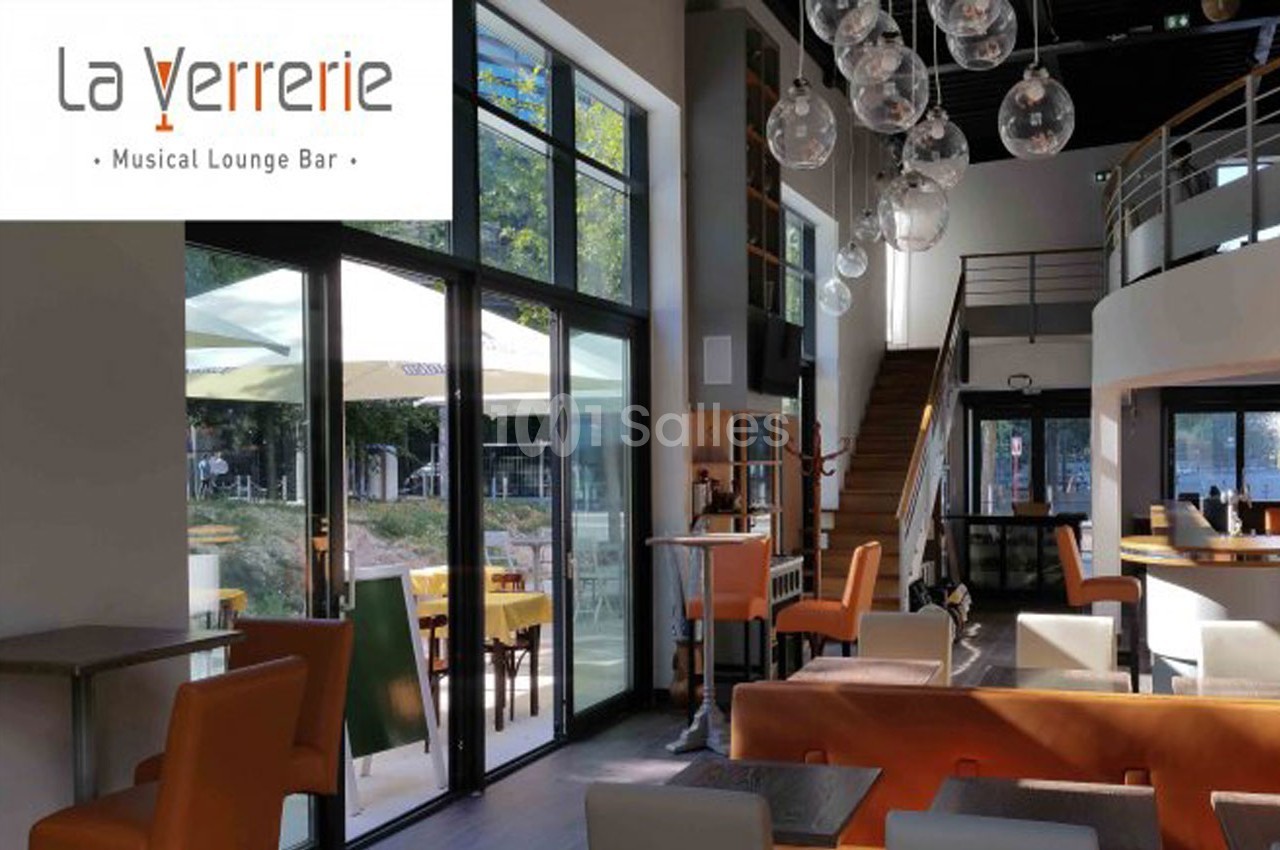 Intérieur lumineux d'un lounge bar avec grandes baies vitrées, mobilier moderne et luminaires suspendus.