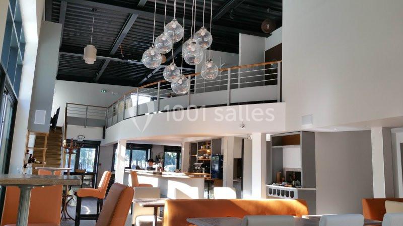 Intérieur lumineux d'un restaurant moderne avec mezzanine, mobilier contemporain et suspensions en verre.