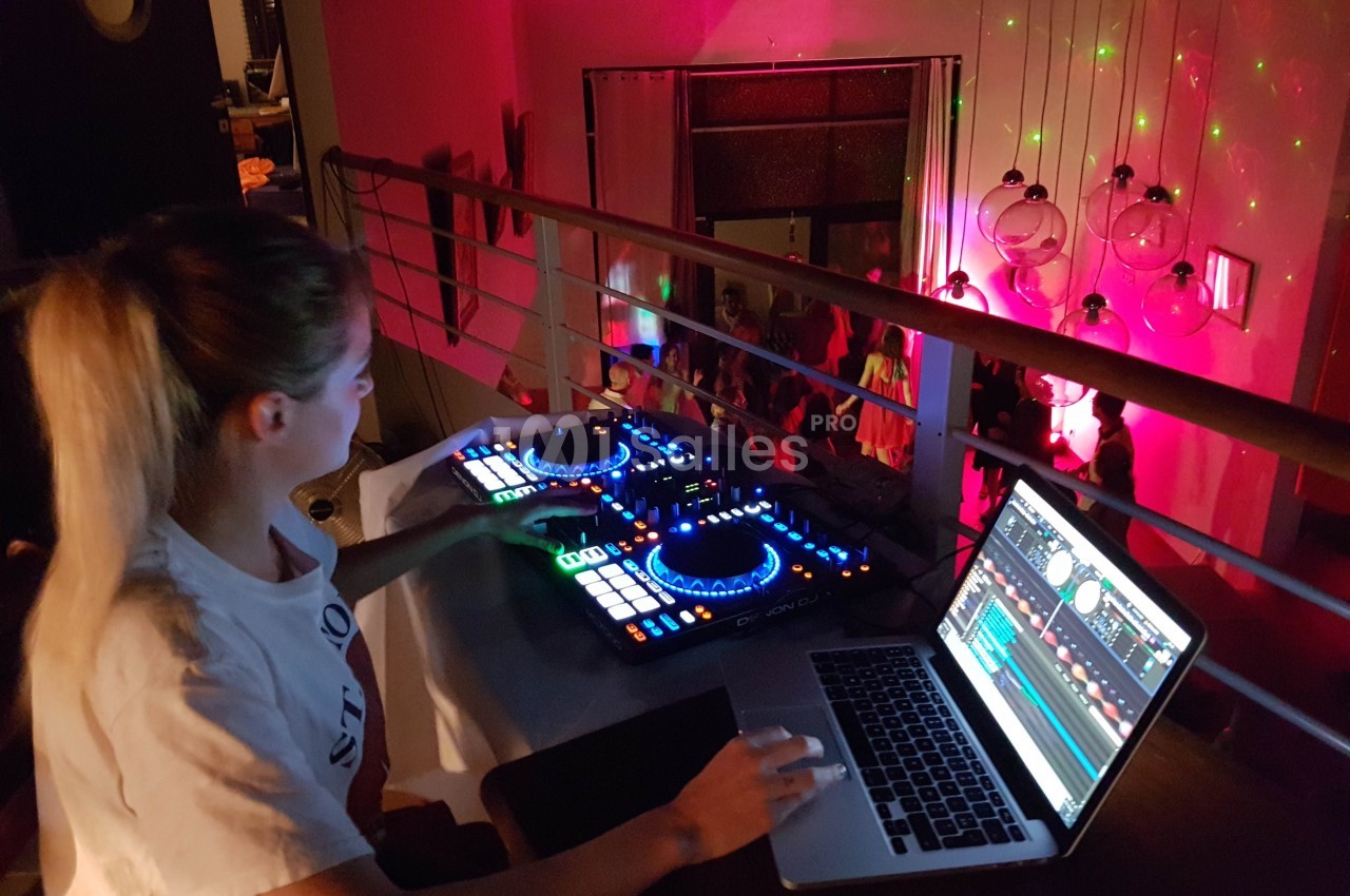 Une DJ mixe de la musique sur une console lumineuse, accompagnée d'un ordinateur, dans une ambiance festive.