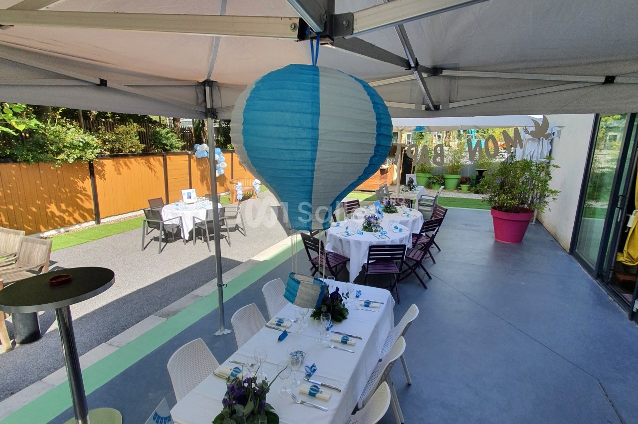 Tables dressées sous une tente avec décoration bleue et blanche, dans un espace extérieur aménagé.
