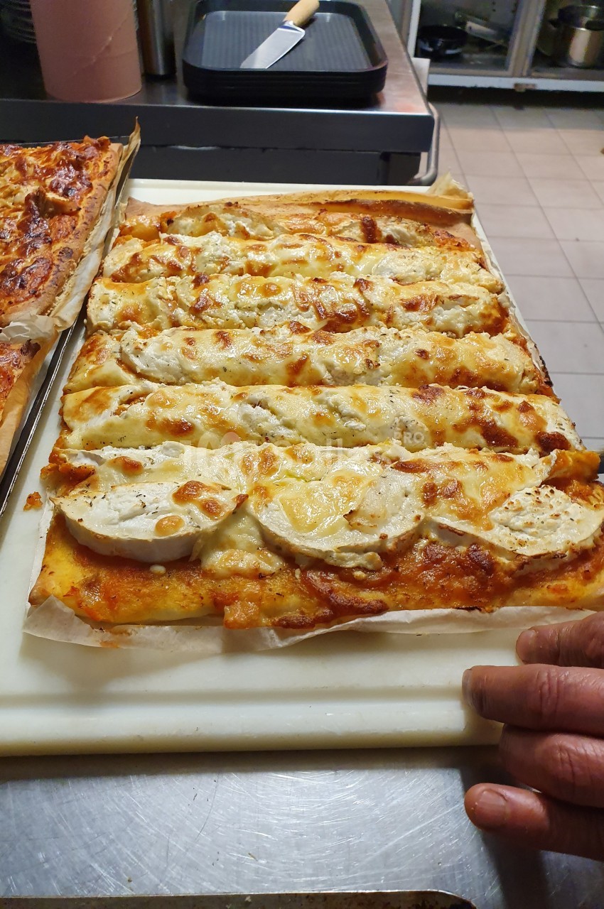 Pizza rectangulaire garnie de fromage de chèvre et de sauce tomate, posée sur une planche dans une cuisine.