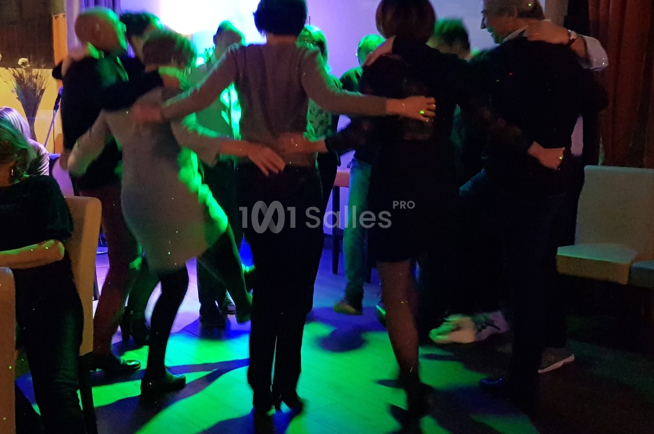Groupe de personnes dansant en cercle dans une ambiance lumineuse tamisée avec des reflets verts.