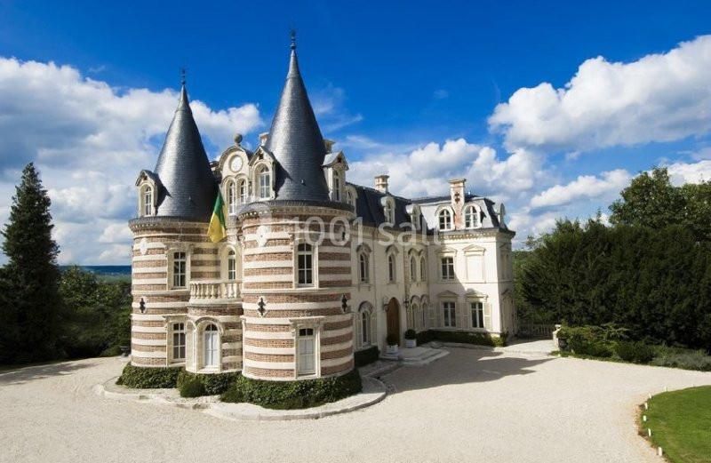 Château en briques rouges et blanches avec tourelles, entouré de végétation sous un ciel partiellement nuageux.