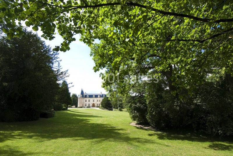 Vue d'un parc verdoyant avec pelouse, arbres et un bâtiment de style château en arrière-plan.