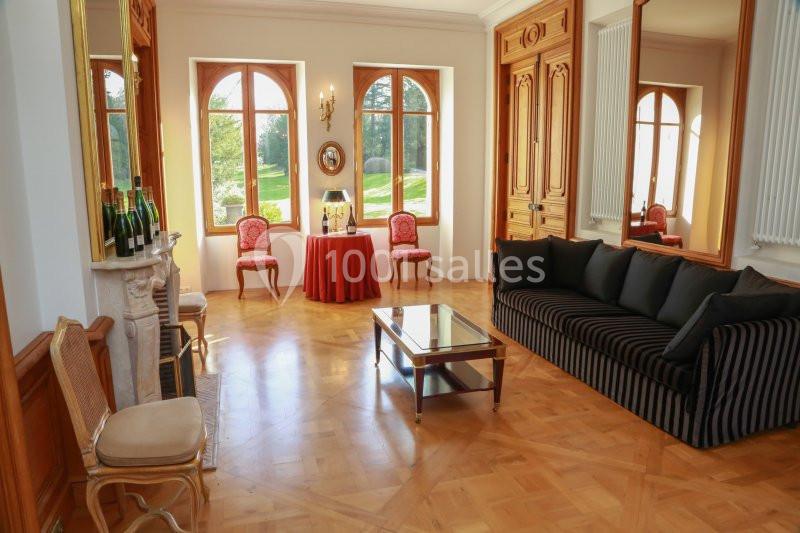 Salon lumineux avec parquet, canapé rayé noir, cheminée, table basse et grandes fenêtres donnant sur un jardin.