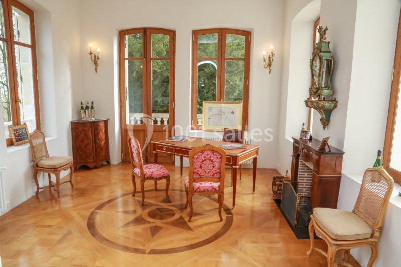 Bureau élégant avec parquet en bois, meubles anciens, chaises tapissées et grandes fenêtres donnant sur un jardin.