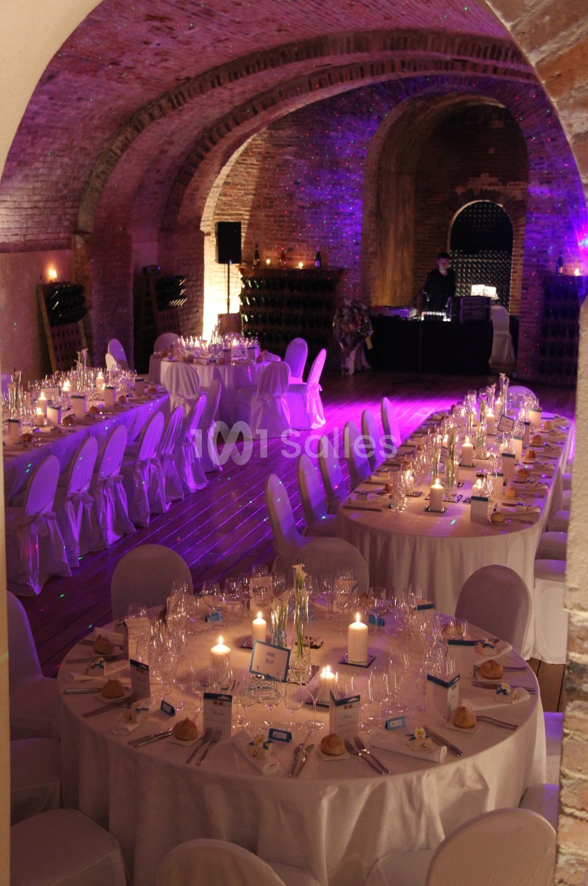 Salle voûtée en briques aménagée pour un dîner, avec tables rondes décorées et éclairage tamisé.