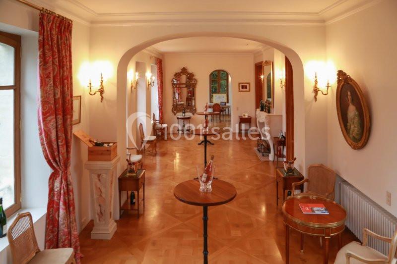 Salon lumineux avec parquet en bois, meubles classiques, tableaux, rideaux rouges et éclairage mural chaleureux.