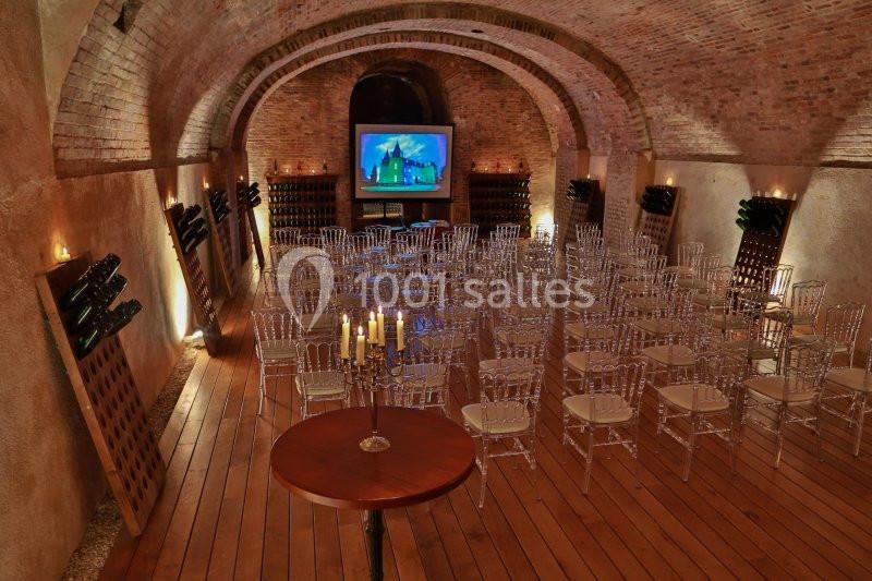 Salle voûtée en briques avec chaises transparentes disposées face à un écran de projection, éclairage tamisé.