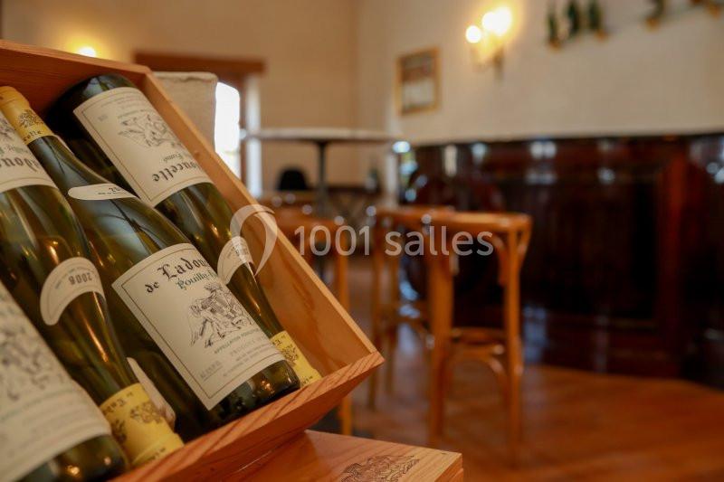 Des bouteilles de vin blanc dans une caisse en bois, avec un bar en bois et des tabourets en arrière-plan.