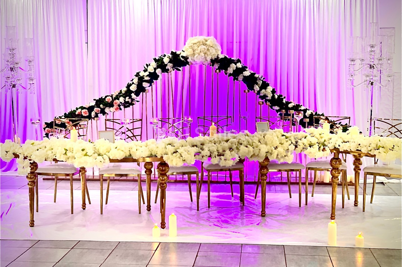 Table décorée pour un événement avec des fleurs blanches et noires, éclairage violet et rideaux en arrière-plan.