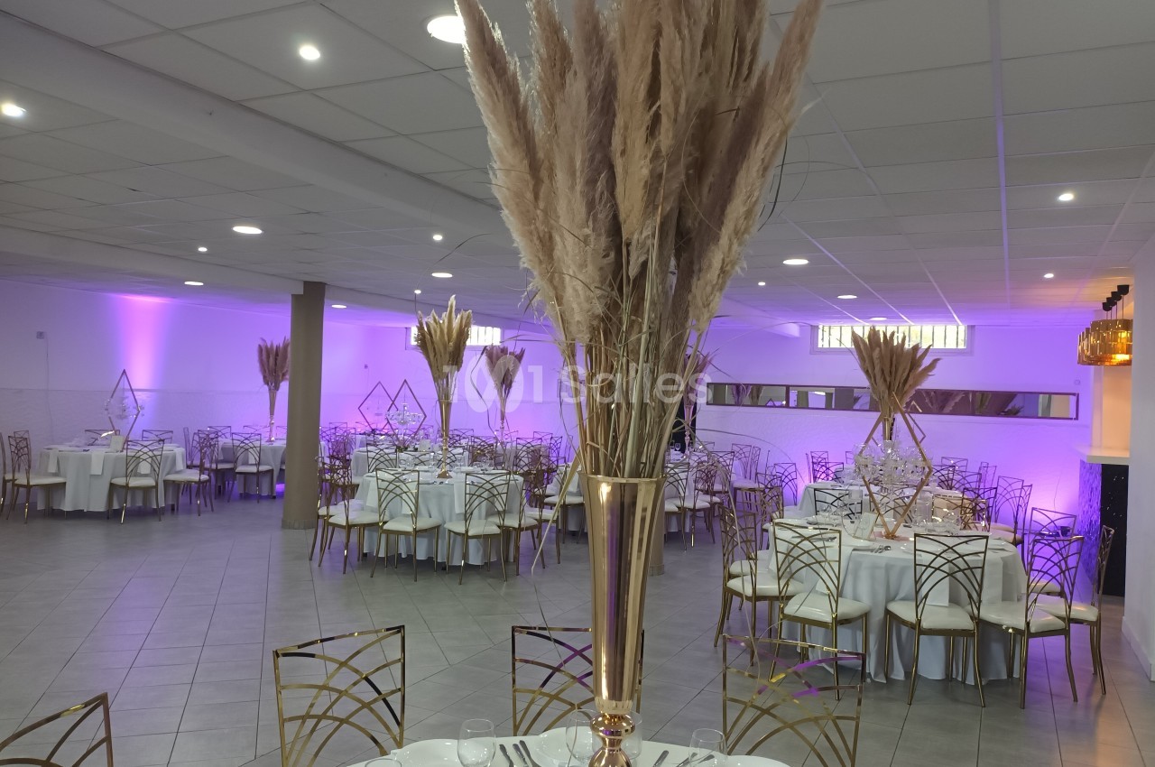 Salle de réception décorée avec des tables rondes, nappes blanches, chaises dorées et centres de table en herbes de la pampa.