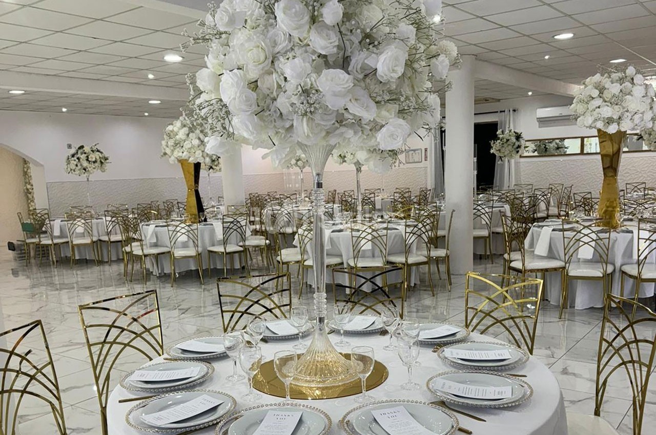 Salle de réception élégante avec tables décorées de nappes blanches, vaisselle raffinée et centres de table fleuris.