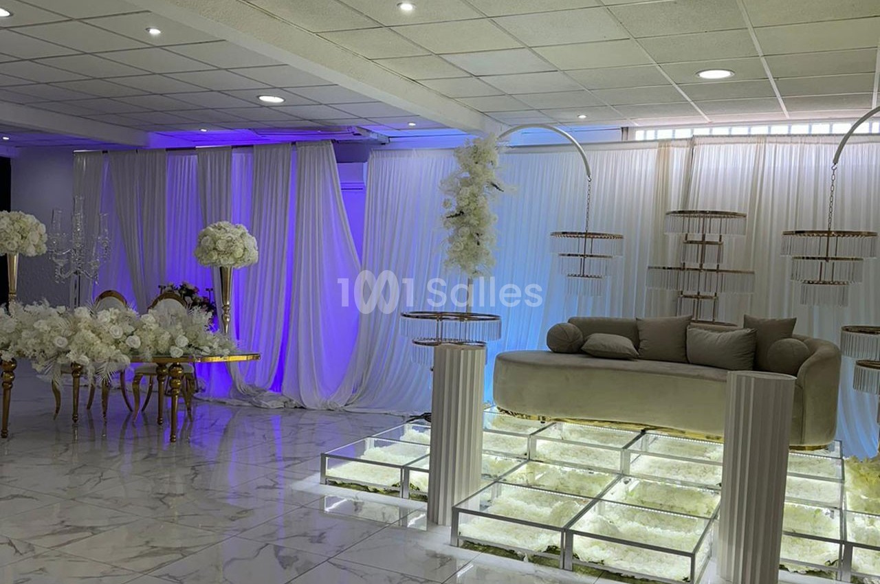 Salle de réception décorée avec des rideaux blancs, des fleurs, un canapé beige et un sol en verre illuminé.