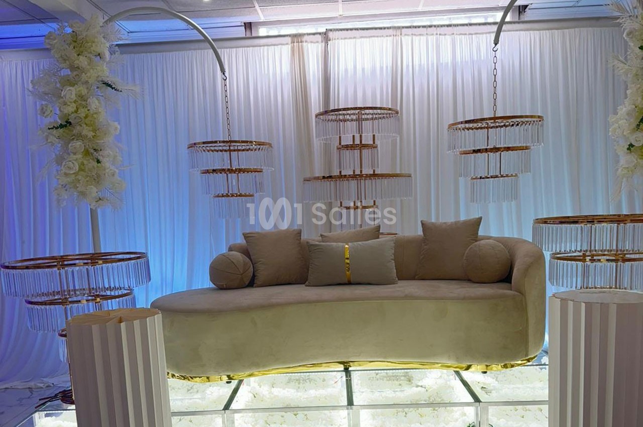 Canapé beige incurvé avec coussins, entouré de lustres suspendus et de colonnes décorées de fleurs blanches.