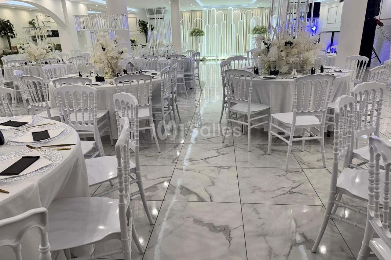 Salle de réception élégante avec tables rondes décorées de fleurs blanches et chaises blanches sur un sol en marbre.