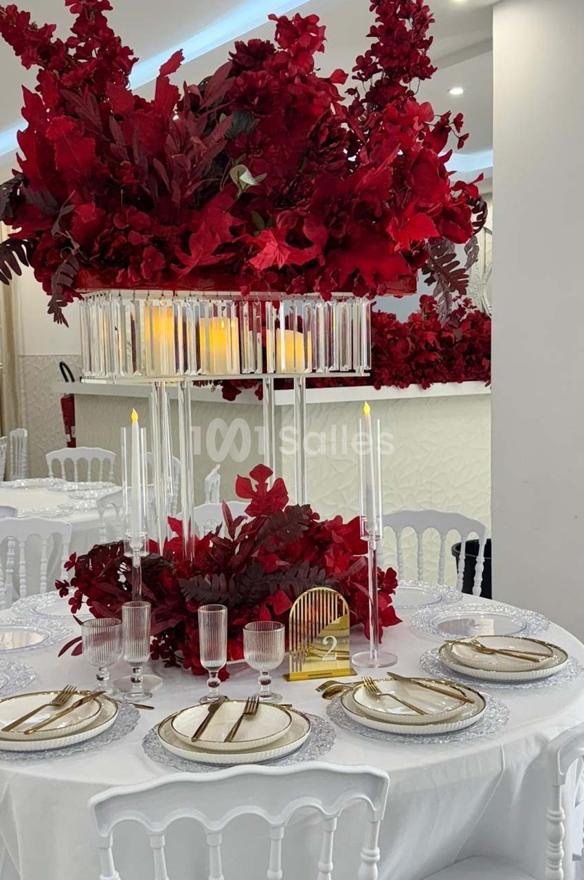 Table élégamment dressée avec vaisselle raffinée, bougies et centre de table composé de fleurs rouges abondantes.