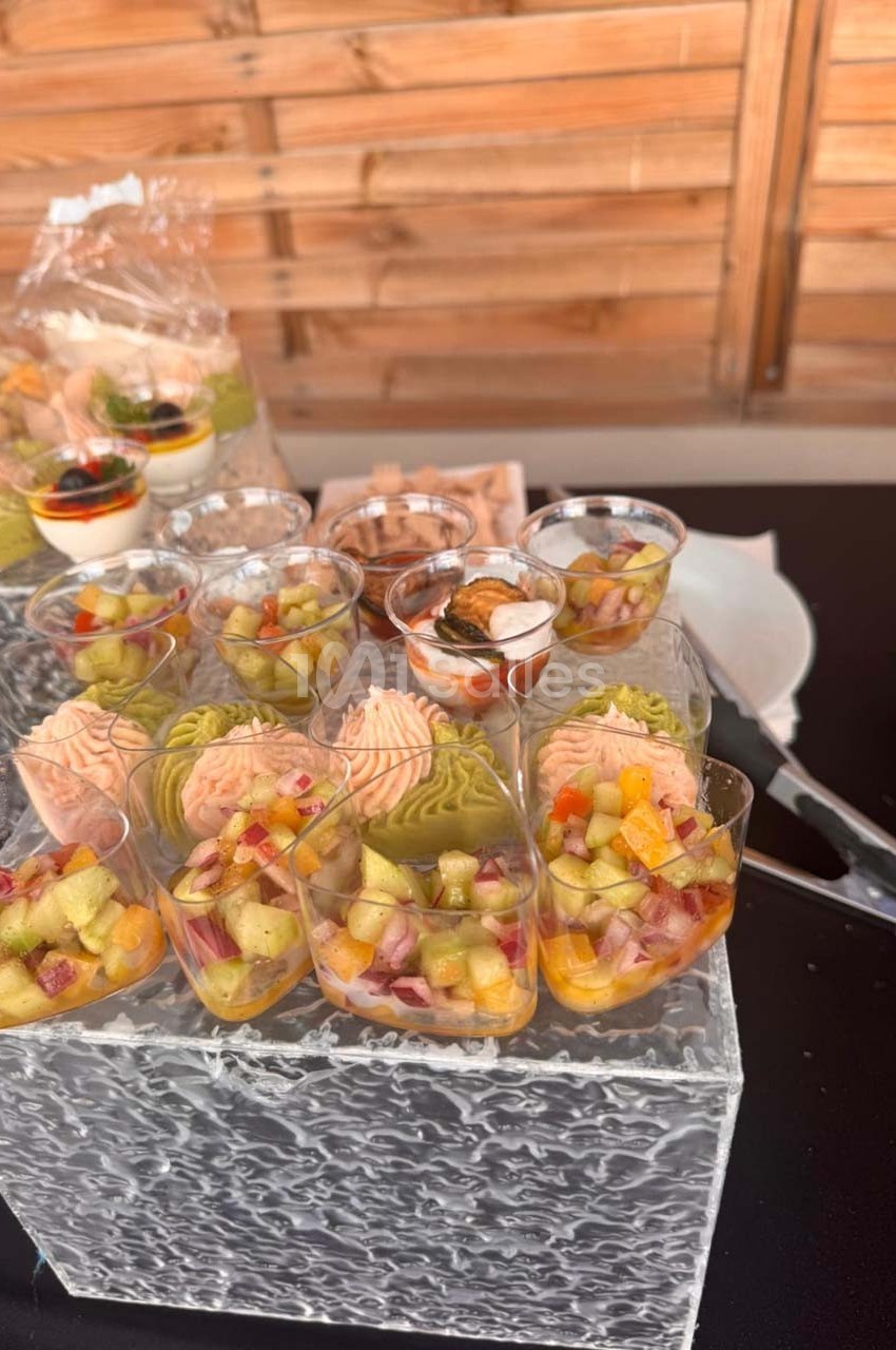 Verrines colorées de légumes et saumon disposées sur un présentoir en verre, avec d'autres amuse-bouches en arrière-plan.