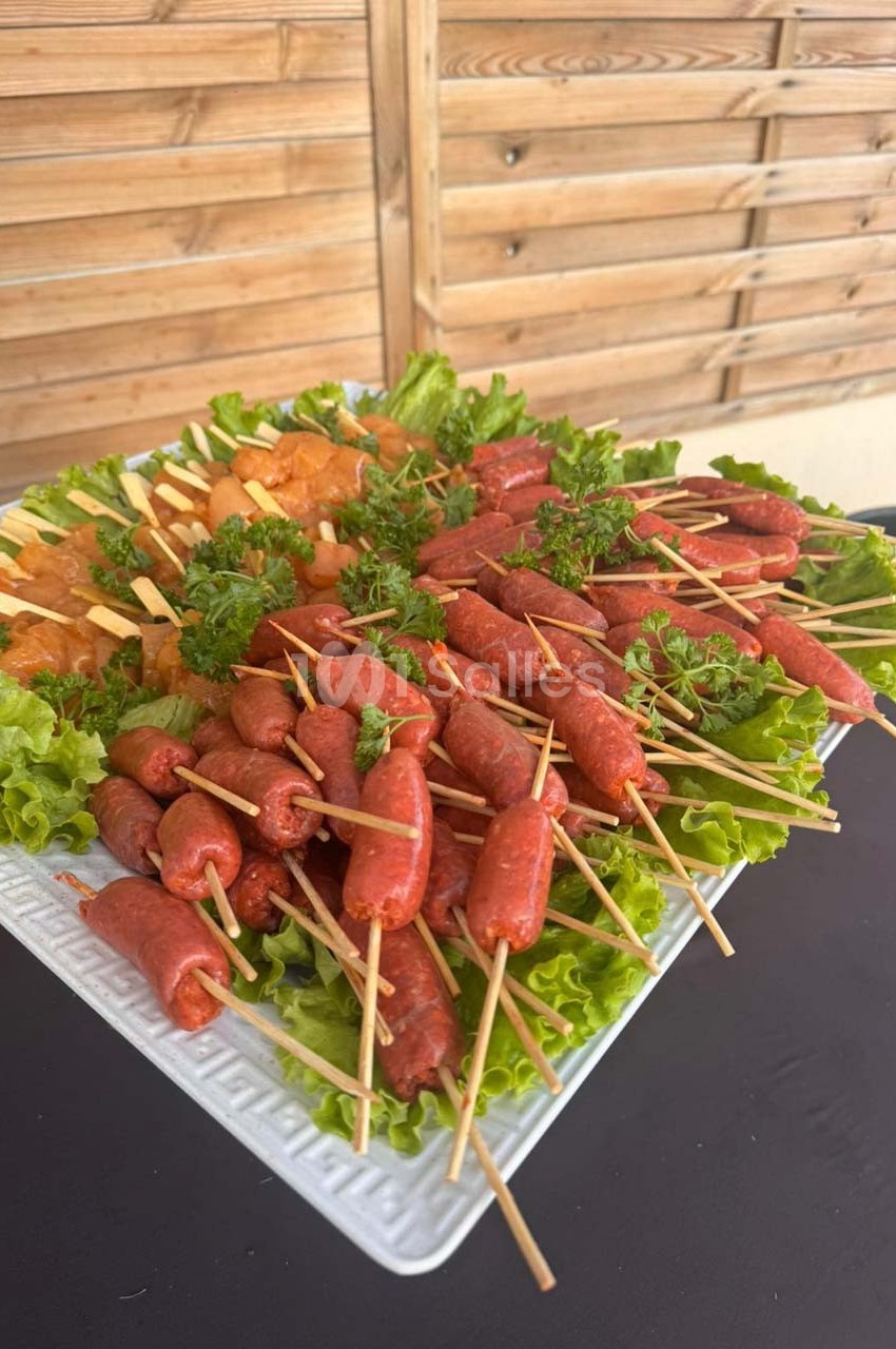 Plateau de brochettes variées avec saucisses et fromage, décoré de feuilles de laitue et de persil.