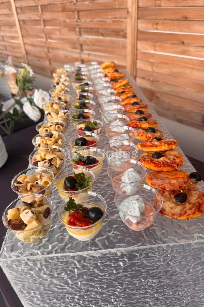 Buffet de verrines et amuse-bouches variés disposés en rangées sur une table avec fond en bois.