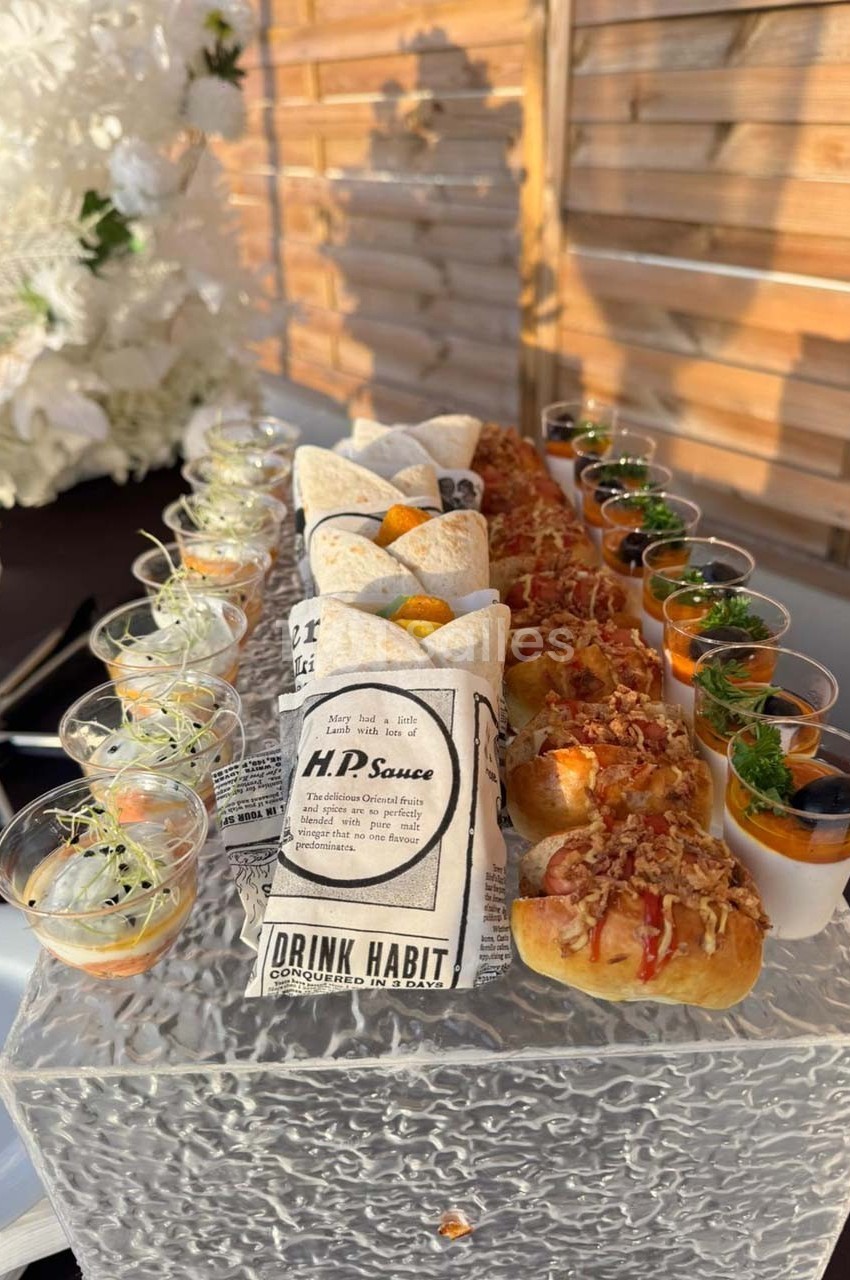 Plateau de bouchées variées comprenant wraps, mini hot-dogs garnis et verrines, présenté sur une table élégante.