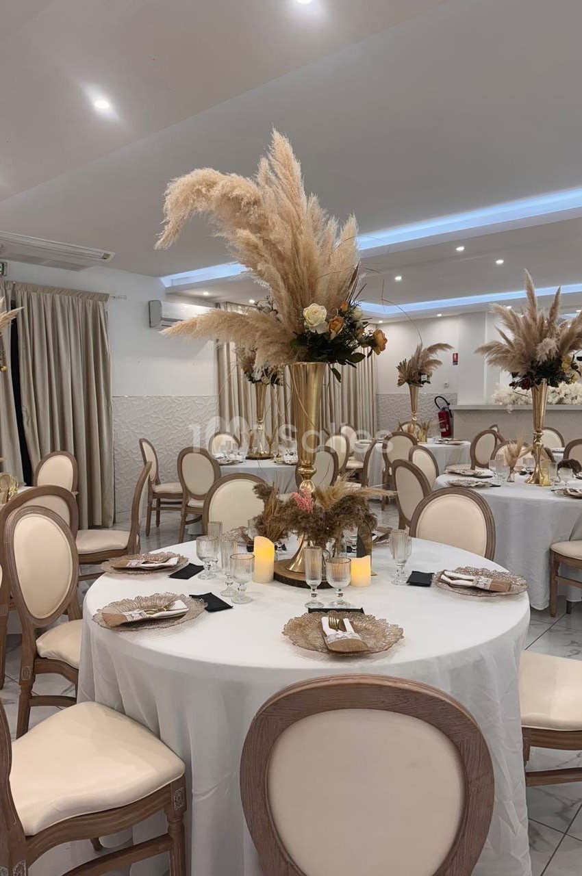 Salle de réception élégante avec tables rondes décorées de centres de table en pampas et bougies.