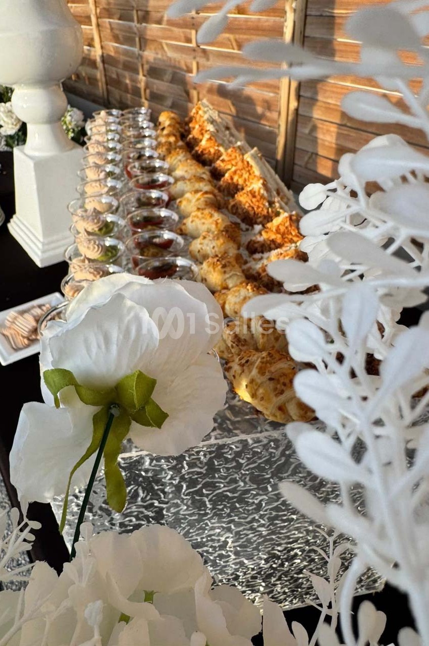 Buffet de verrines et amuse-bouches alignés sur une table, décorée de fleurs blanches en premier plan.