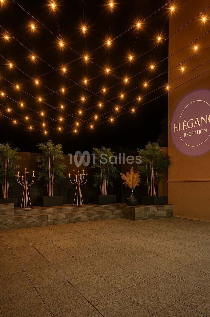 Guirlandes lumineuses suspendues au-dessus d'une terrasse avec plantes, chandeliers et un mur affichant ’Élégance Réception’.