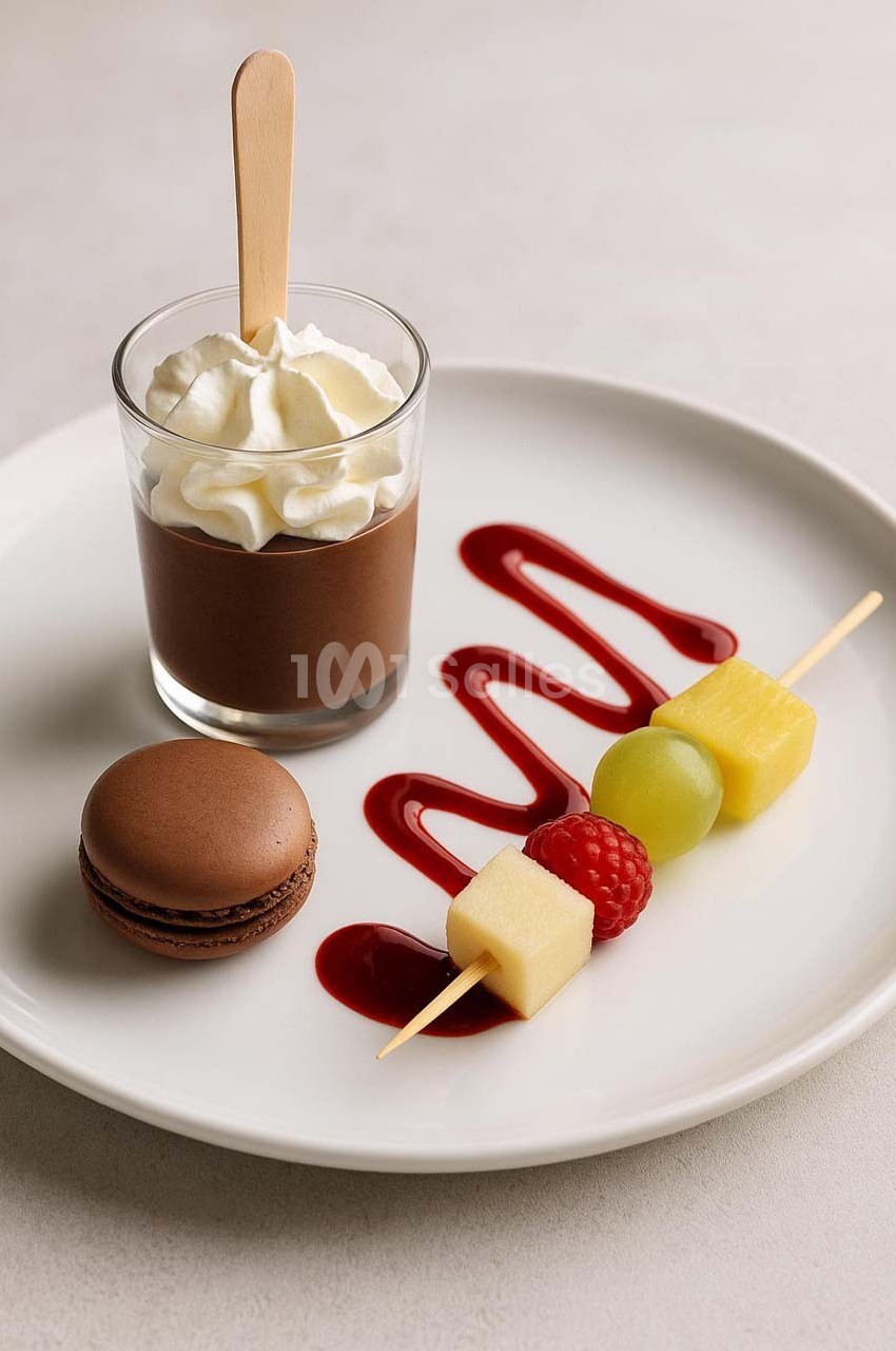 Dessert composé d'une mousse au chocolat, d'un macaron, de fruits sur brochette et d'un coulis rouge sur une assiette…