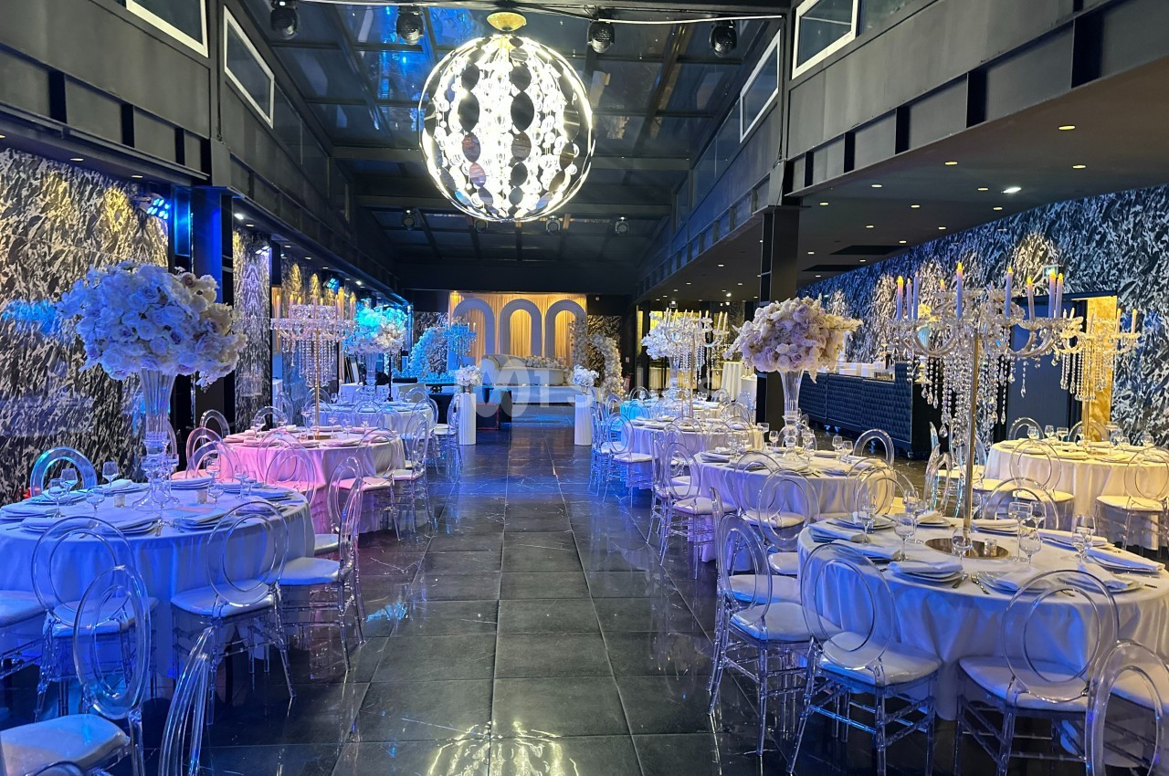 Salle de réception élégante avec tables décorées de nappes blanches, chandeliers et arrangements floraux sous un grand…