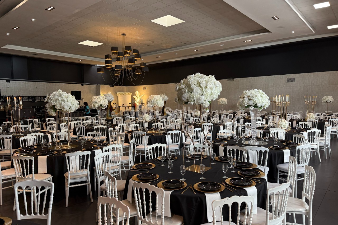 Salle de réception élégamment décorée avec des tables noires, des chaises blanches et des centres de table floraux blancs.